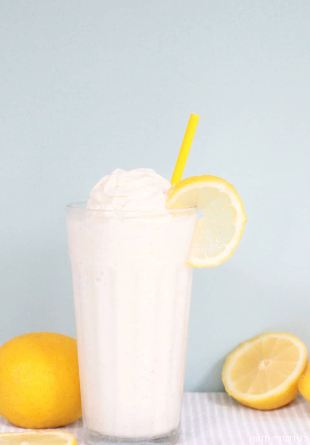 Frosted Lemonade or Frozen Lemonade in a glass with whipped cream on top, a yellow straw and lemon slice on the side.