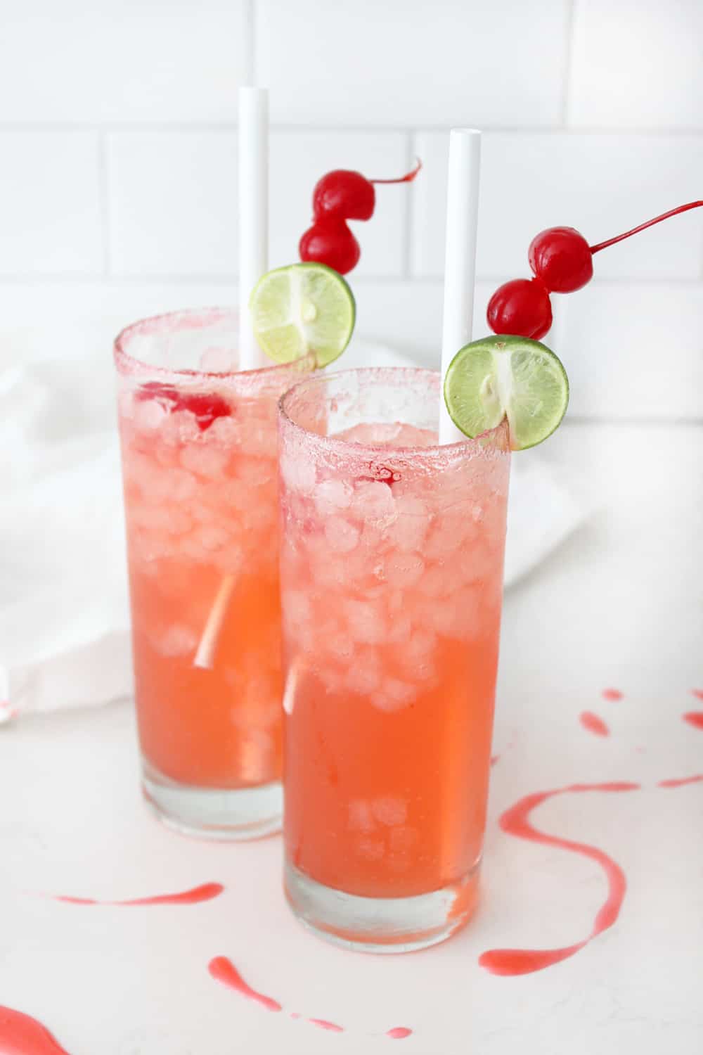 Two glasses of cherry limeade with cherries and limes on drink picks.