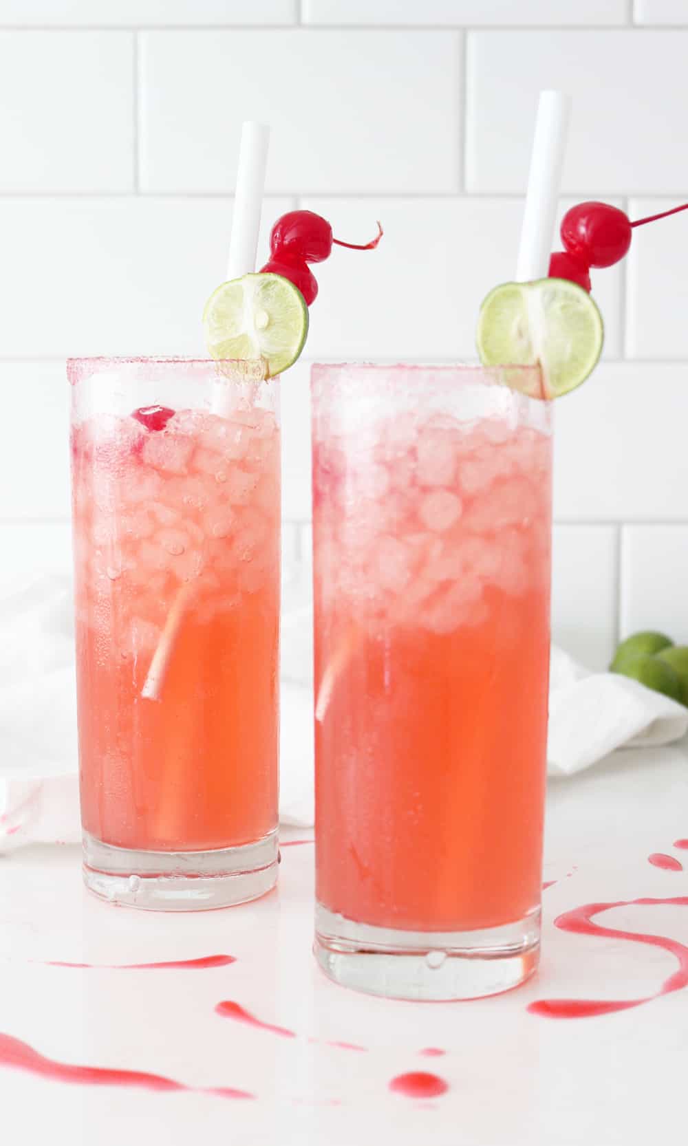 cherry limeade in two clear glasses with drink picks and cherries on top