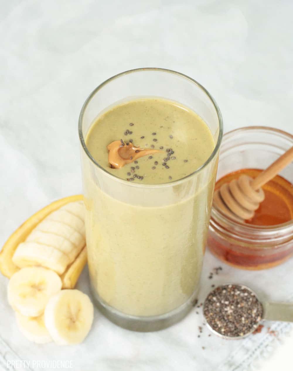 Chocolate Peanut Butter smoothie in a tall glass with peanut butter and chia seeds on top, honey, banana and chia seeds around the glass.