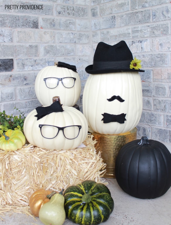 No-Carve Pumpkins wearing glasses, hats, bows and mustaches on a hay bail. Fall porch decoration.