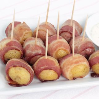 Bacon Wrapped Potatoes with toothpicks on a white plate with creamy dill sauce on the side.