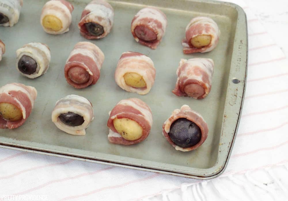 Potatoes wrapped in bacon before baking on a cooking sheet.