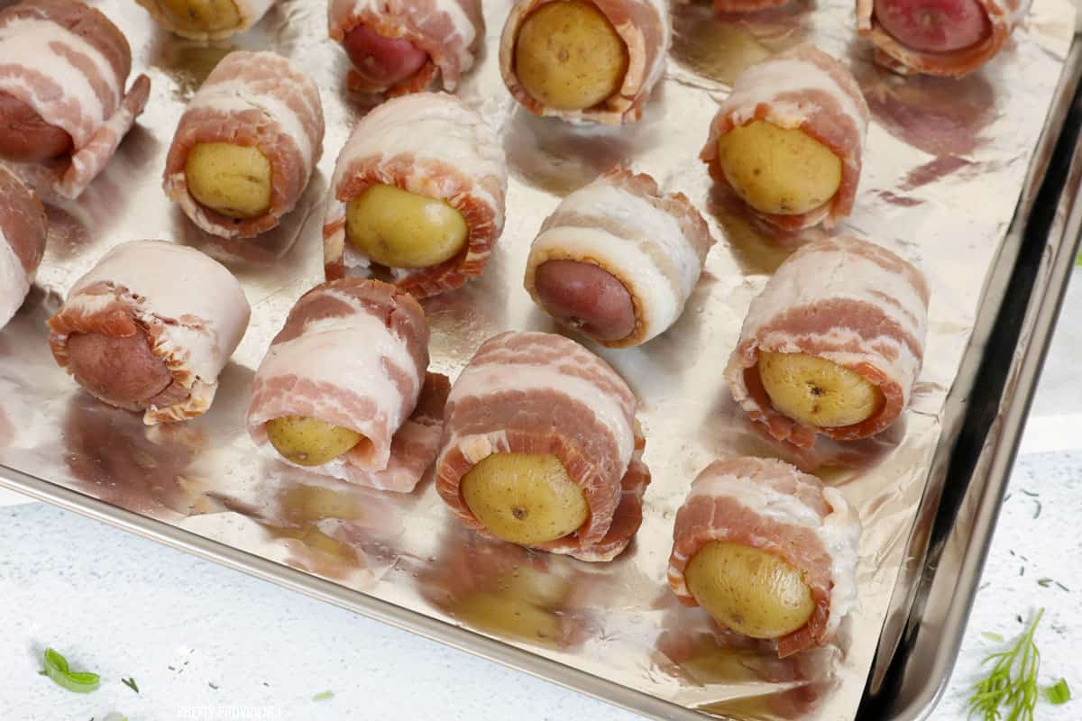 Potatoes wrapped in bacon before baking on a cooking sheet.