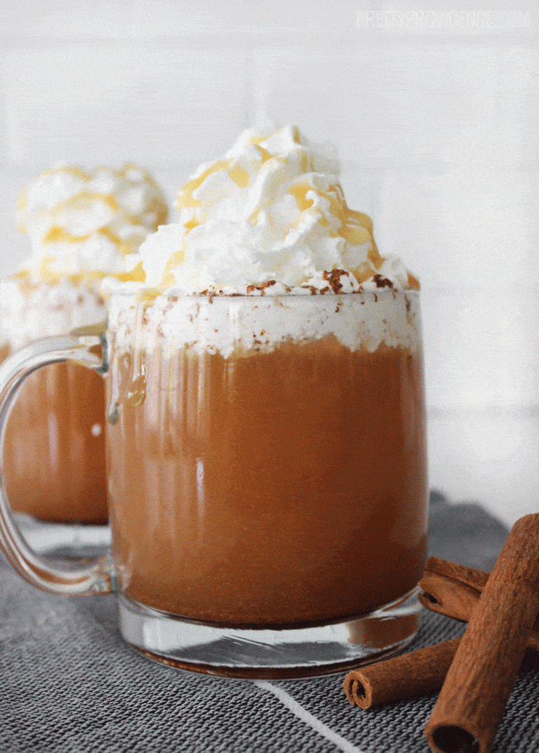 copycat caramel apple cider topped with whipped cream and caramel next to cinnamon sticks on a dark towel