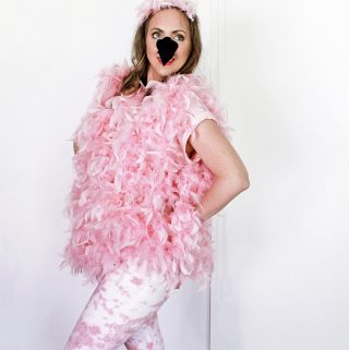 Woman wearing a flamingo costume for Halloween with pink boas, a felt flamingo nose, pink and white pants.