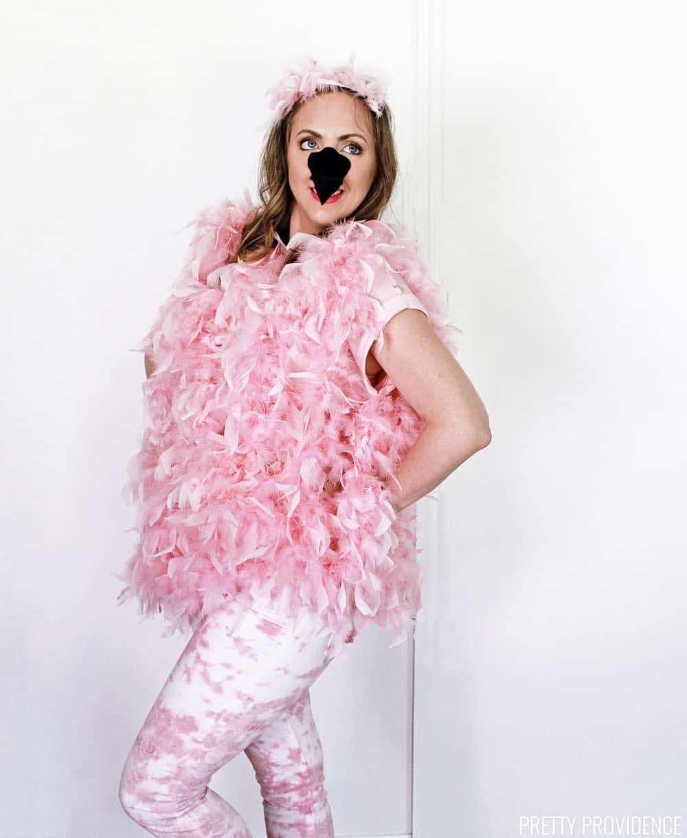 Woman wearing a flamingo costume for Halloween with pink boas, a felt flamingo nose, pink and white pants.