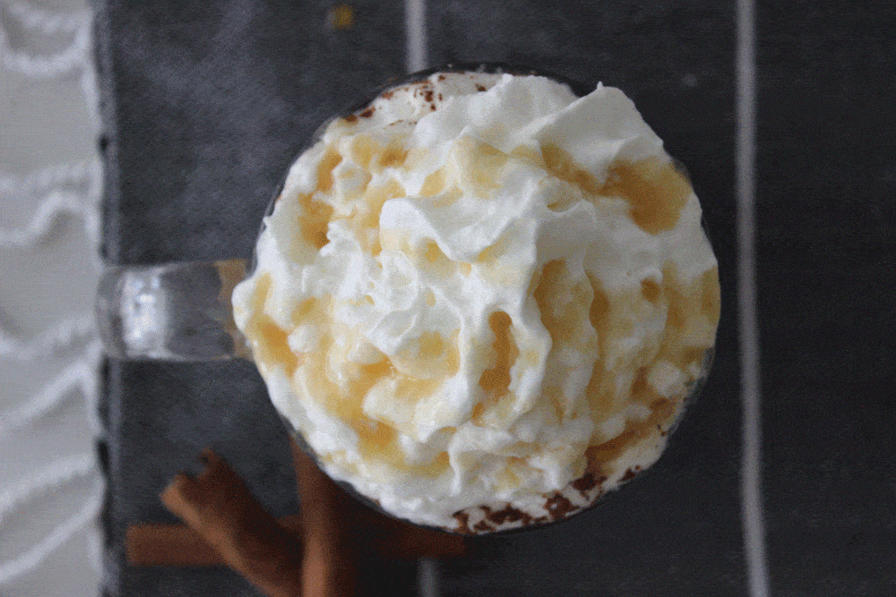 birds eye view of caramel and whipped cream topped caramel apple cider on a black tea towel