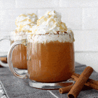 two starbucks caramel apple ciders in clear mugs topped with whipped cream next to cinnamon sticks