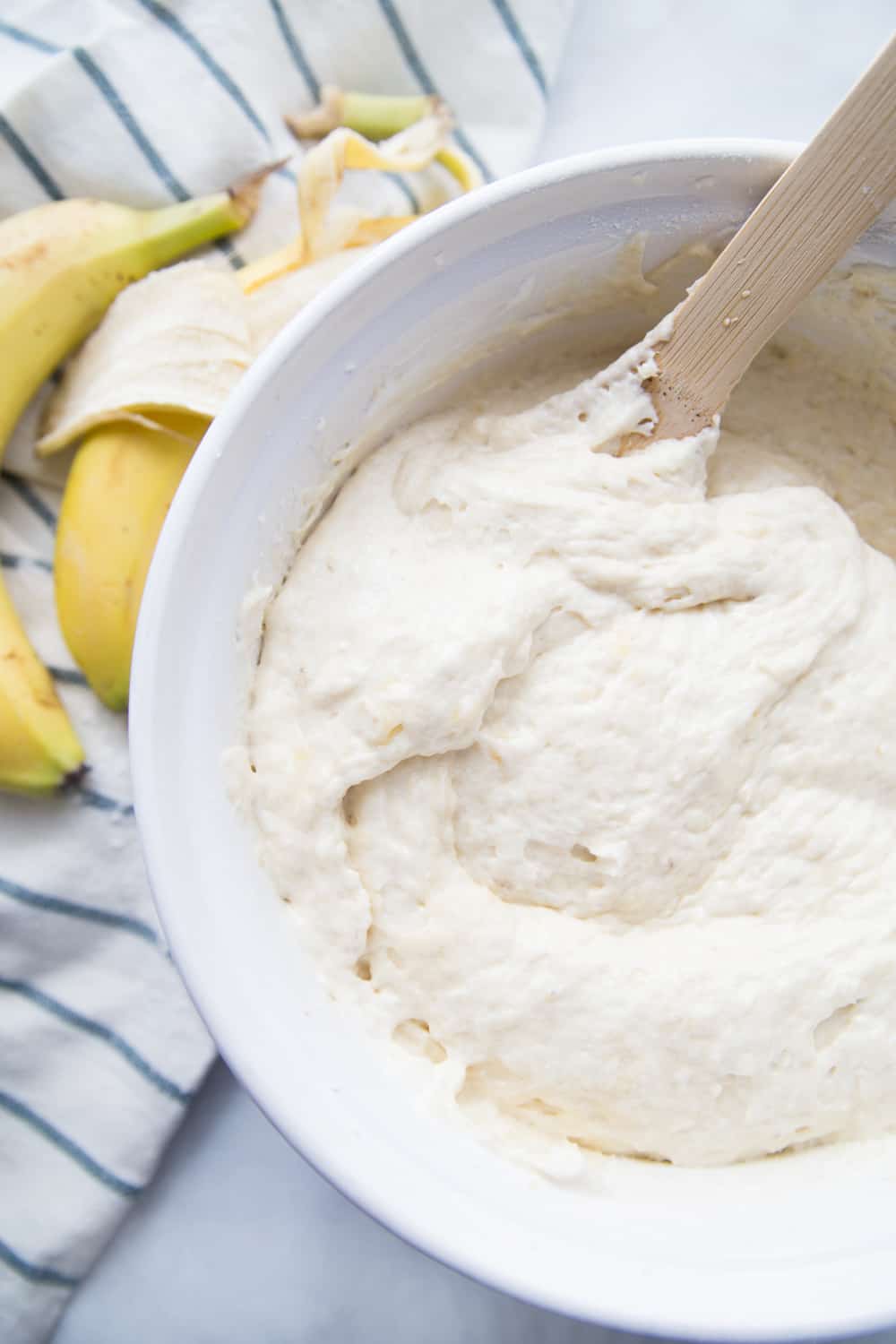 Banana cake batter in a white bowl with a wooden spoon.