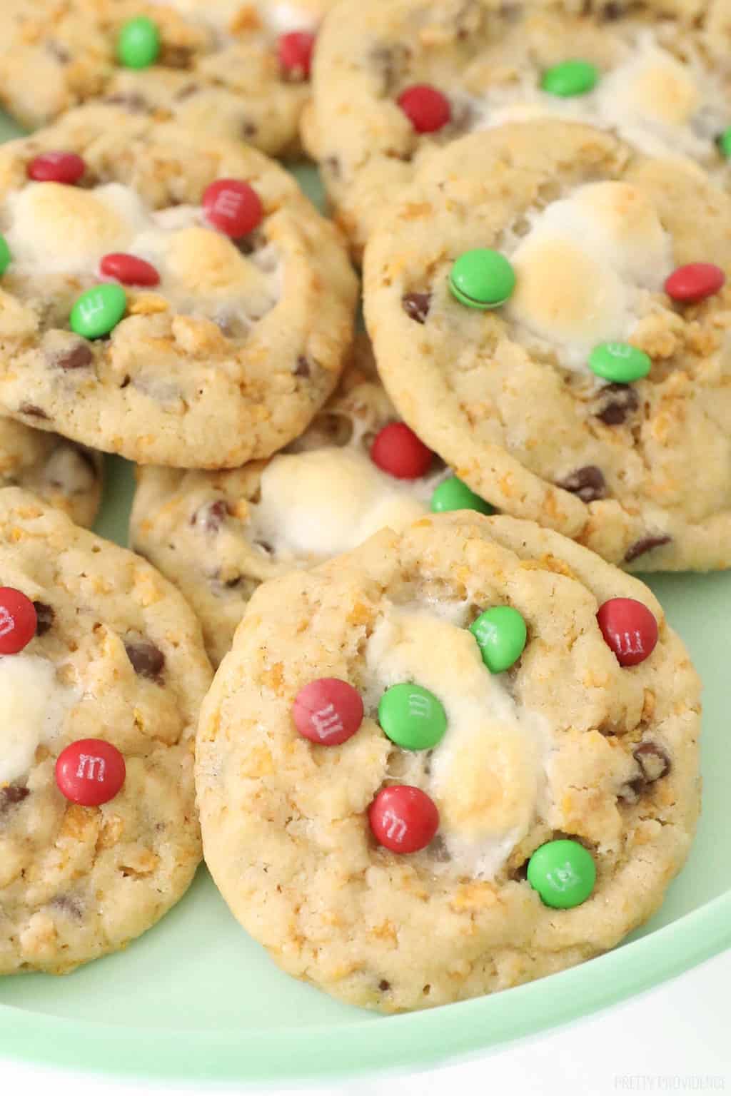 Cookies with red and green mini m&m's, cornflakes and melted marshmallow on a green plate.