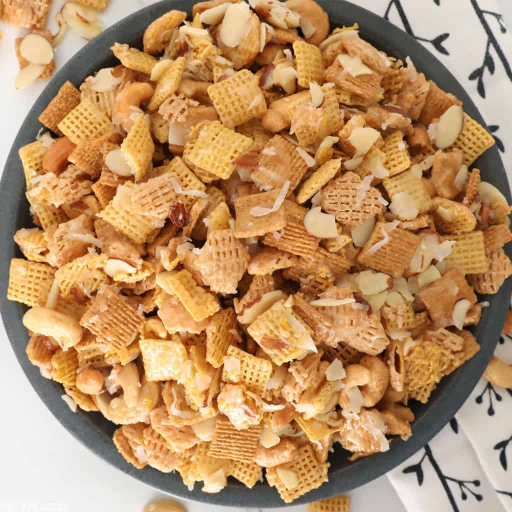 Close up of Sweet Chex mix with cashews, coconut, almonds with sticky caramel coating in a dark blue bowl.