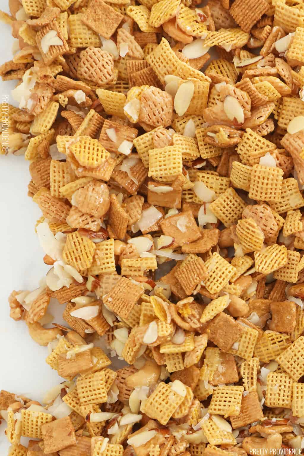 gorp-Close up of Sweet Chex mix with cashews, coconut, almonds with sticky caramel coating on wax paper.