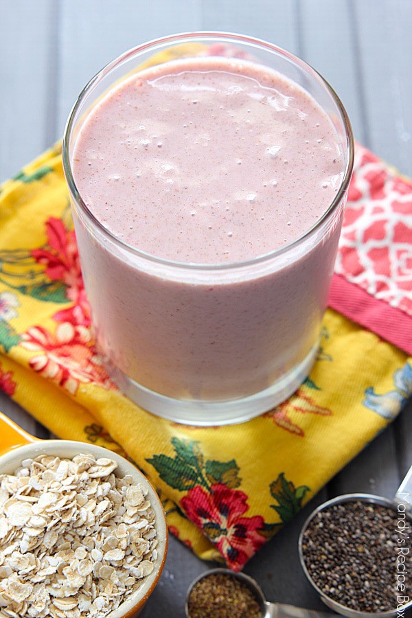 Strawberry Oatmeal Smoothie in a glass with oats, chia seeds and ground flaxseed on top of a yellow floral dish towel.