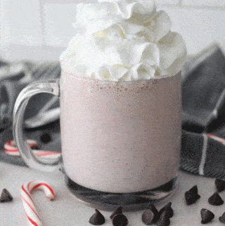 peppermint milkshake in a clear mug surrounded by chocolate chips and candy canes