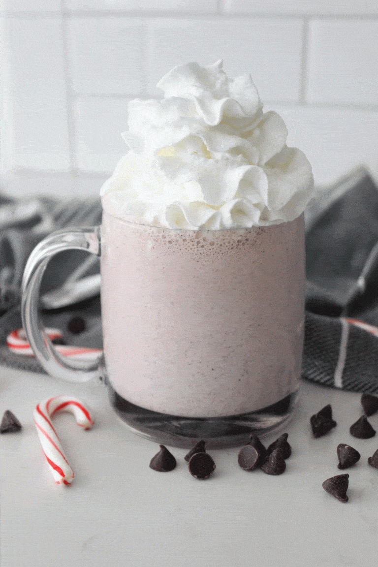 peppermint milkshake in a clear mug surrounded by chocolate chips and candy canes
