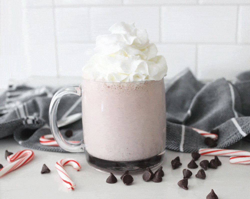 peppermint shake topped with whipped cream surrounded by chocolate chips and candy canes