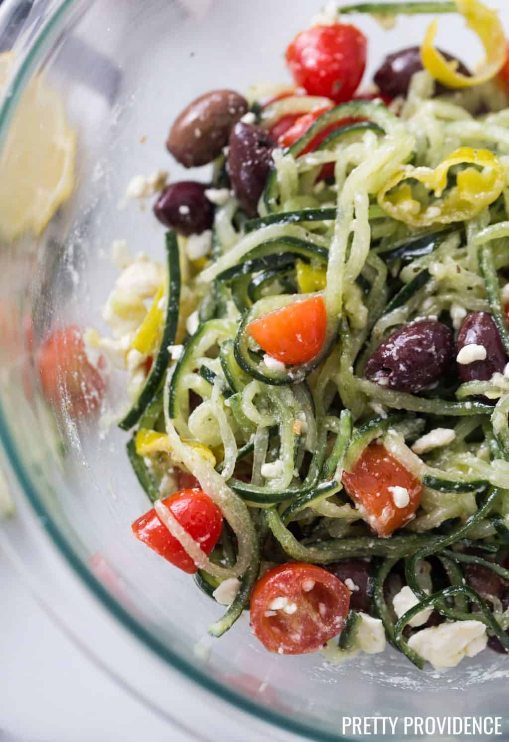 authentic spiralized Greek salad made with cucumber, feta cheese, tomatoes, kalamata olives, greek salad dressing and feta cheese in clear bowl.