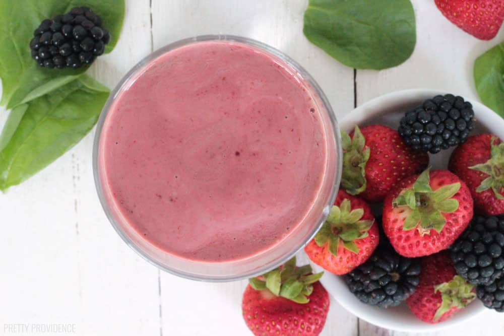 Overhead view of a spinach berry smoothie in a glass, with a small bowl of berries and spinach leaves around it.