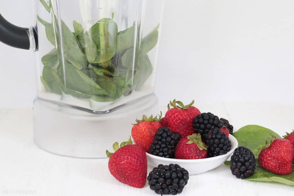 Spinach and Almond milk in a blender, with strawberries, blackberries and spinach in a white bowl next to it.