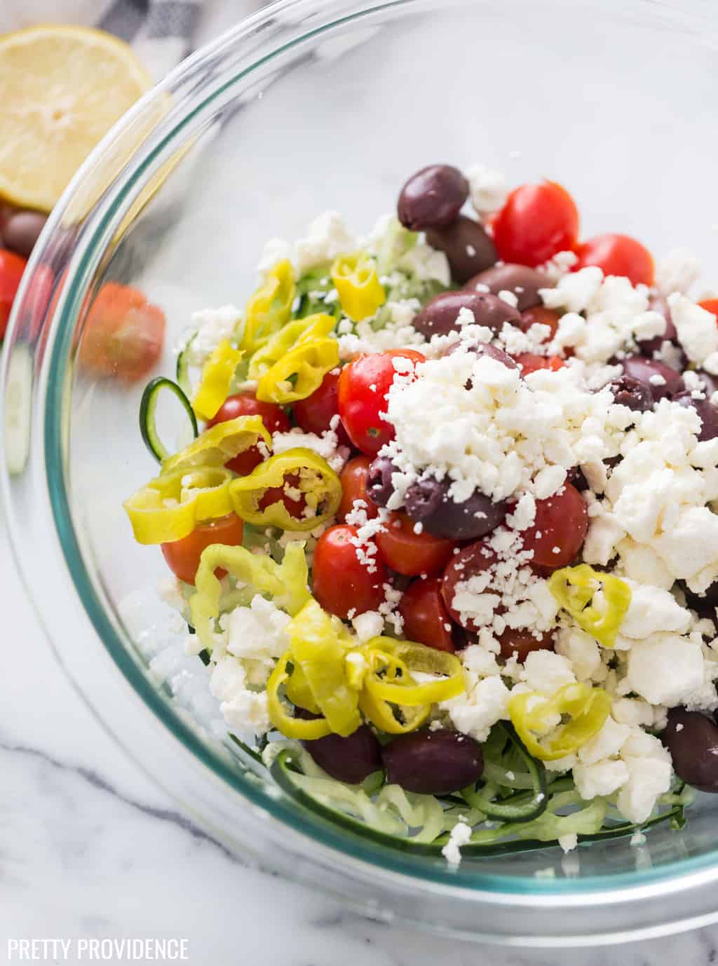 Greek salad ingredients in a bowl with feta cheese, pepperoncini, tomatoes, kalamata olives and spiralized cucumber.