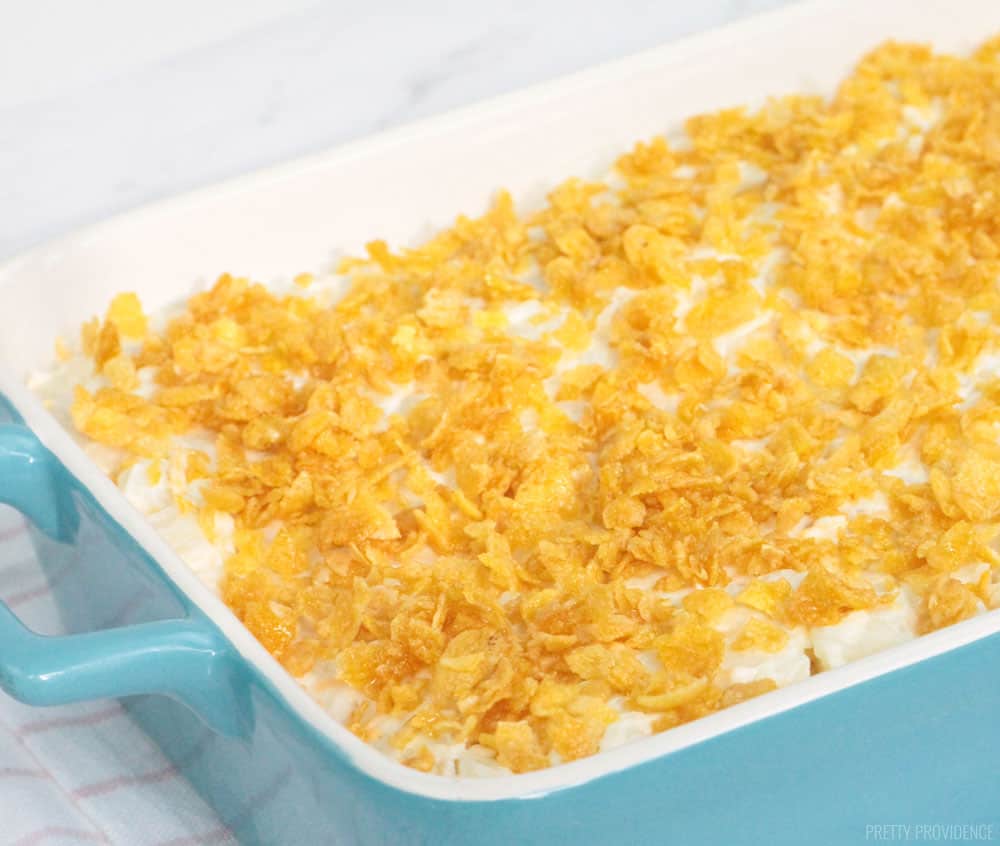 Funeral Potatoes aka cheesy potato casserole with cornflakes on top in a blue 9x13 dish, ready to go in the oven.