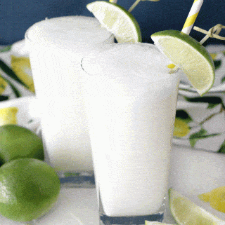 Two glasses of brazilian lemonade garnished with limes against a blue wall