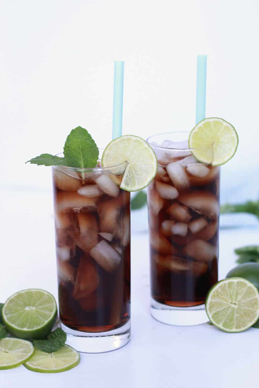 Dirty Dr. Pepper drink with coconut and lime in highball glasses with lime slices and fresh mint as garnish.