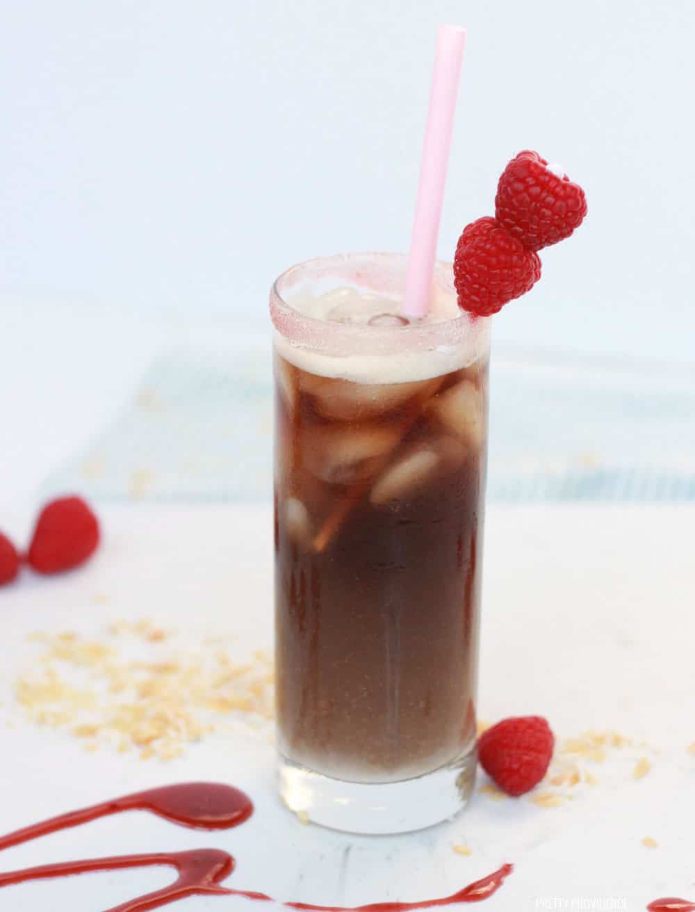 Raspberry Dr. Pepper mocktail in a highball glass with ice cubes and garnished with fresh raspberries.