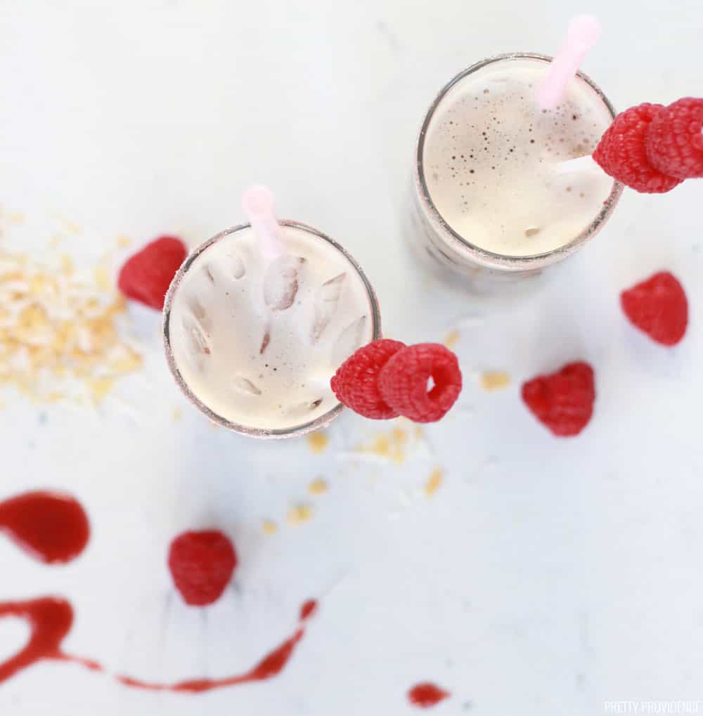Overhead view of two mixed sodas, with raspberry puree in drink and raspberries and coconut flakes as a garnish.
