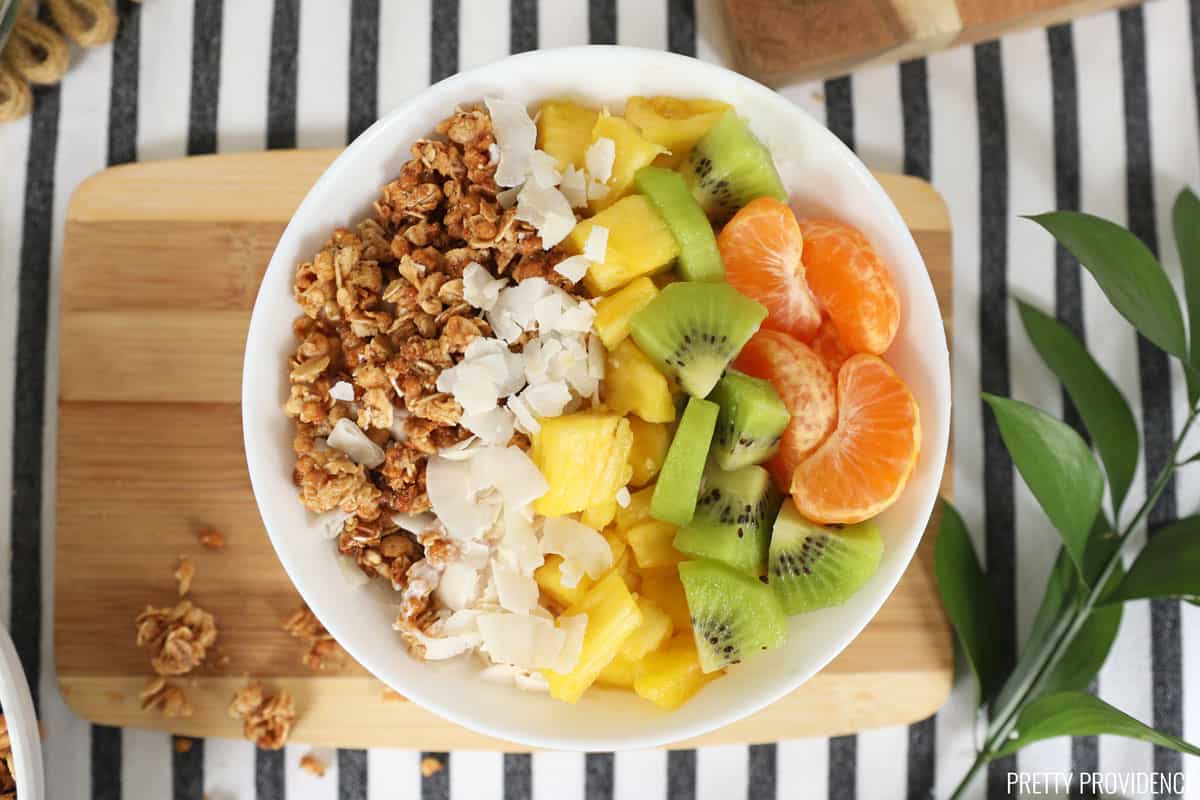 Vanilla yogurt with granola, coconut, pineapple and blueberries in a white bowl. 