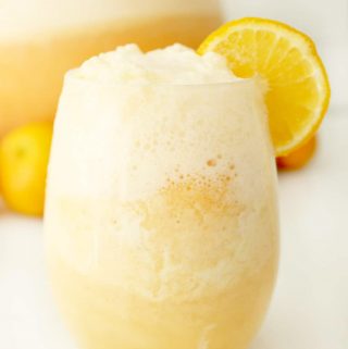 glass of orange sherbet punch with foam on top and an orange slice for garnish