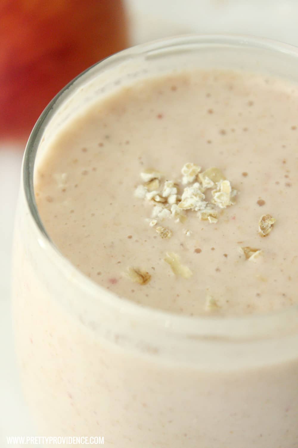 Close up of a strawberry peach smoothie in a glass cup with oats on top.