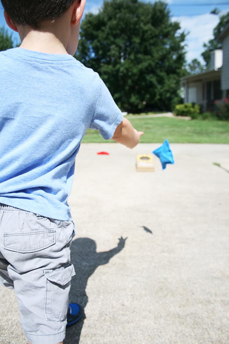 A small child throwing a bean bag toward a mini cornhole board.