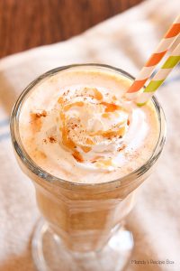 A pumpkin milkshake in a glass with whipped cream and caramel topping.