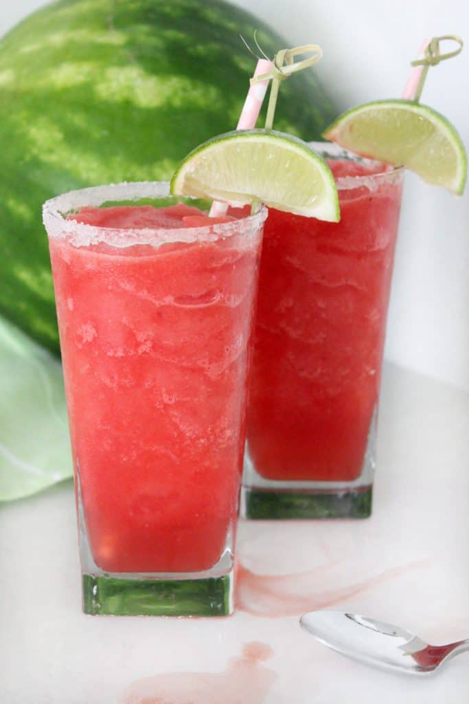 two watermelon slushes in clear glasses in front of a full watermelon