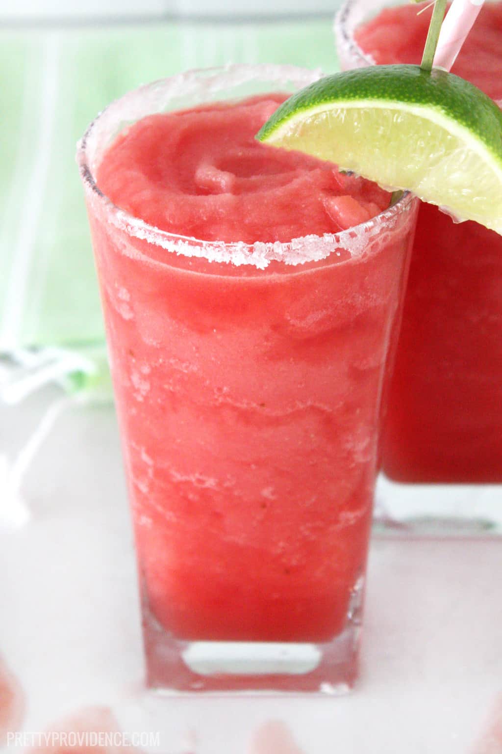 watermelon slush in a tall clear glass garnished with a lime wedge