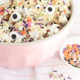 Marshmallow Popcorn in a pink mixing bowl, with Halloween sprinkles and candy eyeballs throughout. Spooky Monster Marshmallow Popcorn!