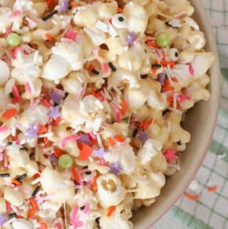 Gooey marshmallow popcorn in a pink bowl with orange, pink, purple and white sprinkles on top.