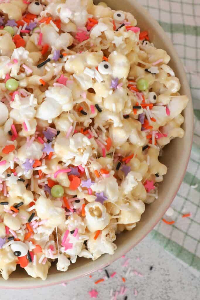 Gooey marshmallow popcorn in a pink bowl with orange, pink, purple and white sprinkles on top.