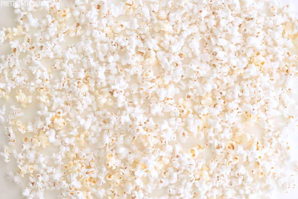 Popped popcorn spread out on top of wax paper on a white countertop.