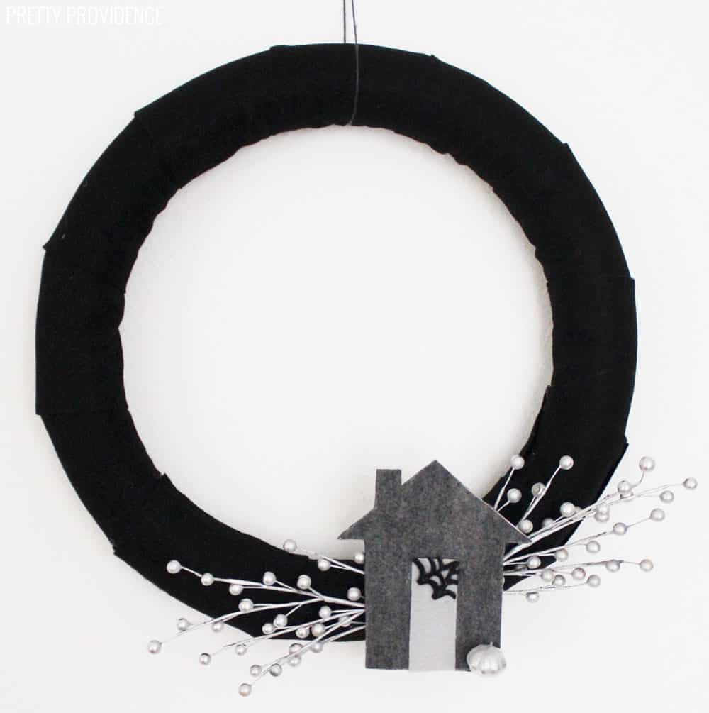 Black Halloween Wreath with a grey felt Haunted House and silver berries hanging on a white wall.