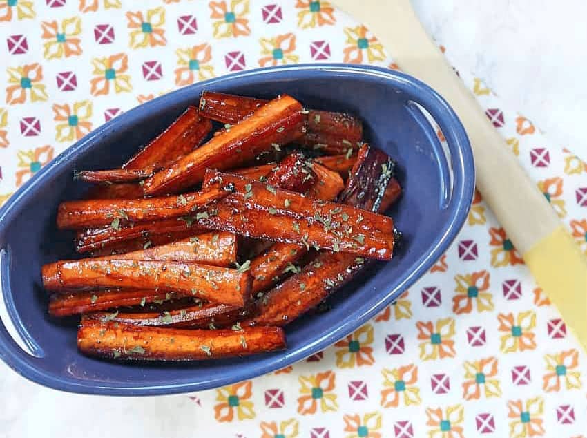 Brown Sugar Balsamic Roasted Carrots in a blue serving dish over a patterned tea towel.