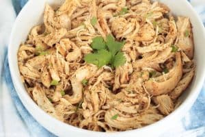 Crockpot shredded chicken for tacos in a white bowl with cilantro on top