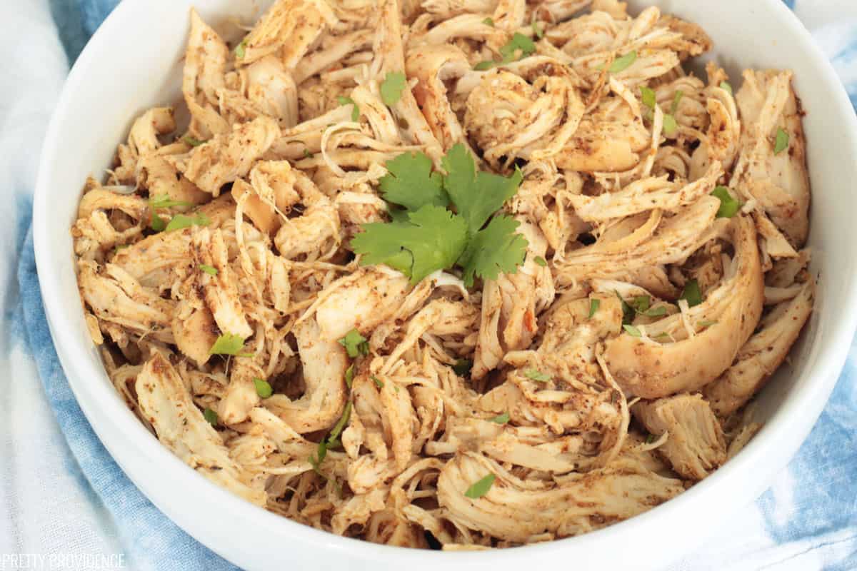 Shredded chicken in a white bowl with cilantro garnish