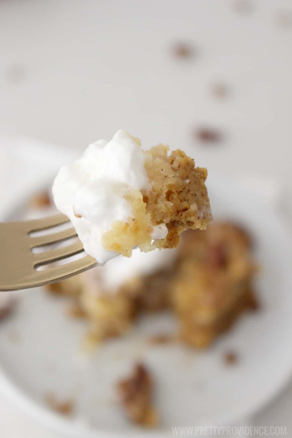 Bite of pumpkin dessert on a fork with whipped cream.