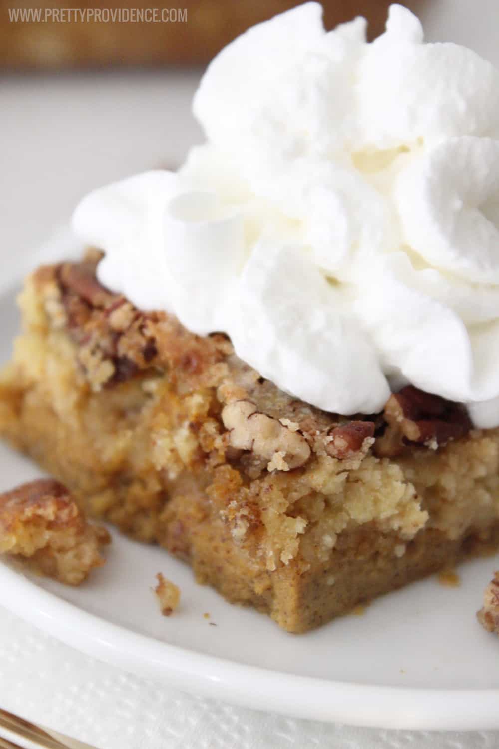 Slice of pumpkin dump cake dessert on a plate, tall whipped cream on top and walnut crumbles on top and sides.