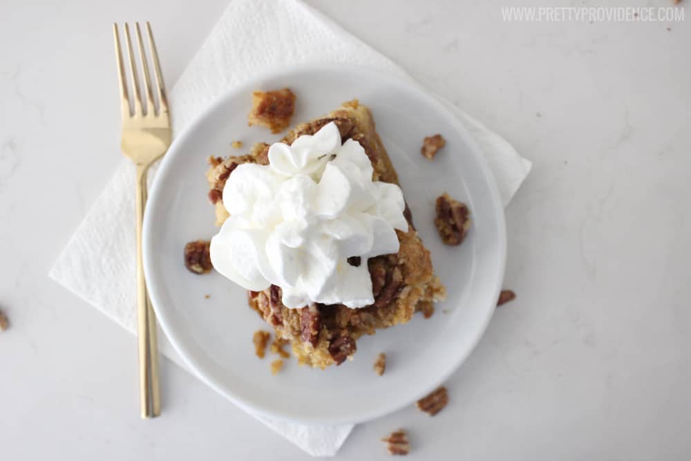 Overhead view of pumpkin dessert, with walnut crunchy topping and whipped cream on a white plate, white napkin and gold fork on the side.