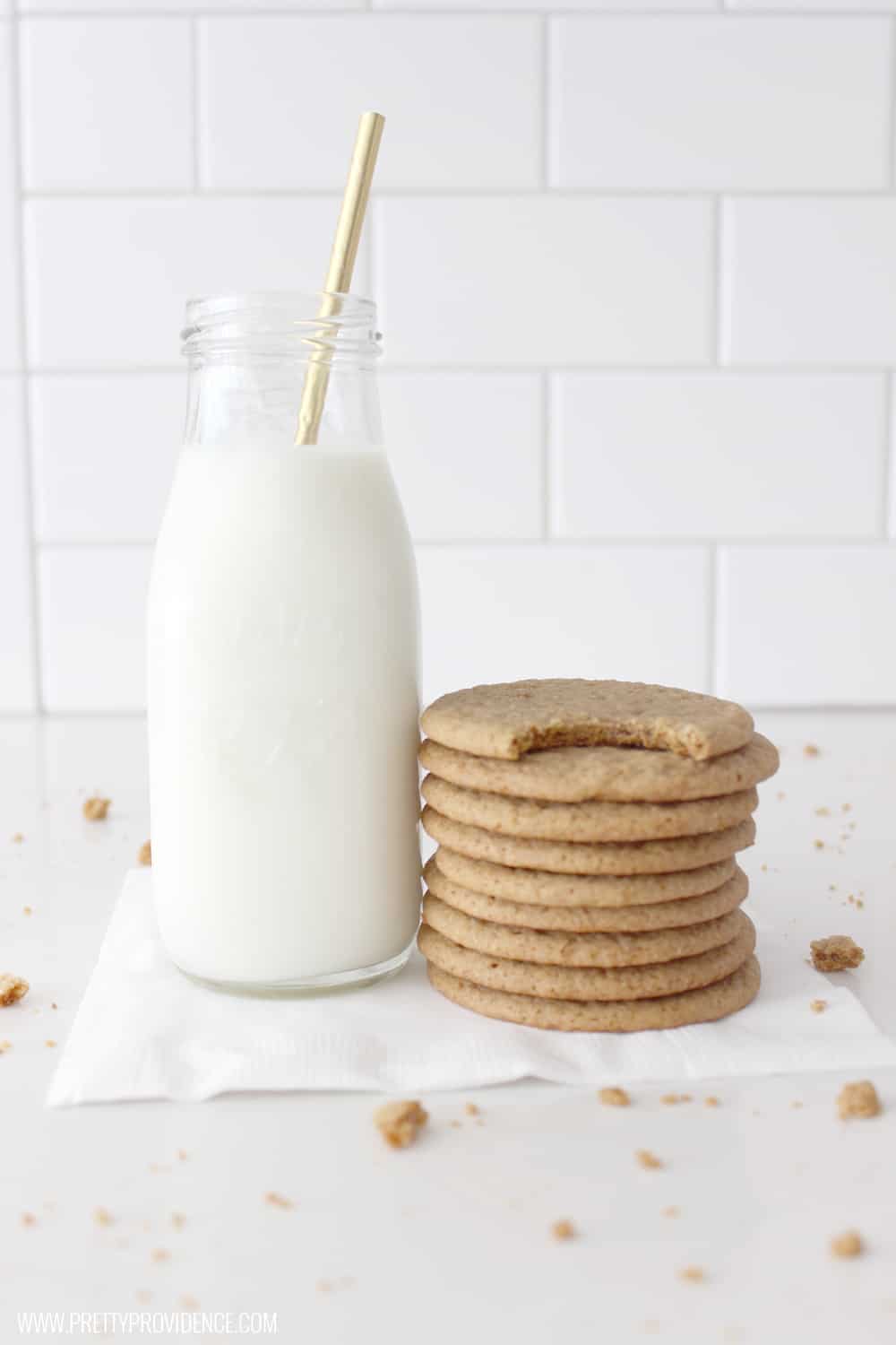 a stack of ginger snaps next to a milk glass with a gold straw and crumbs surrounding