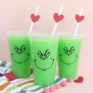 Bright green punch in clear party cups with The Grinch face on them and red hearts on the straws